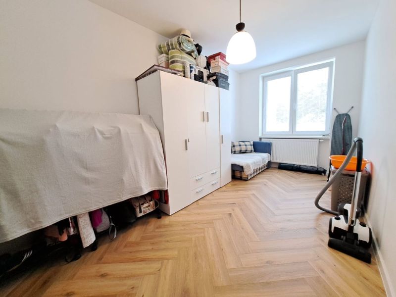A room in a 3-room apartment with a wooden decor floor, a wardrobe, and a vacuum cleaner.