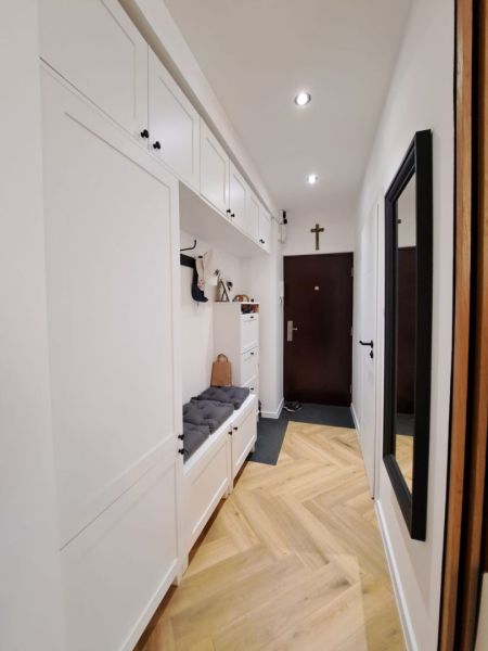 A hallway in a 3-room apartment with a wooden decor floor and white storage cabinets.