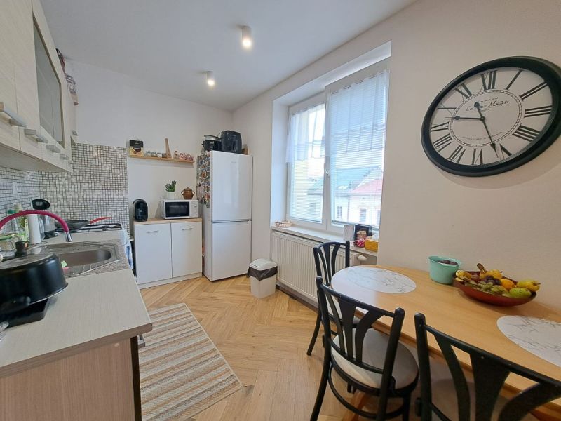 A kitchen in a 3-room apartment with a wooden decor floor, a dining table, and a large clock.
