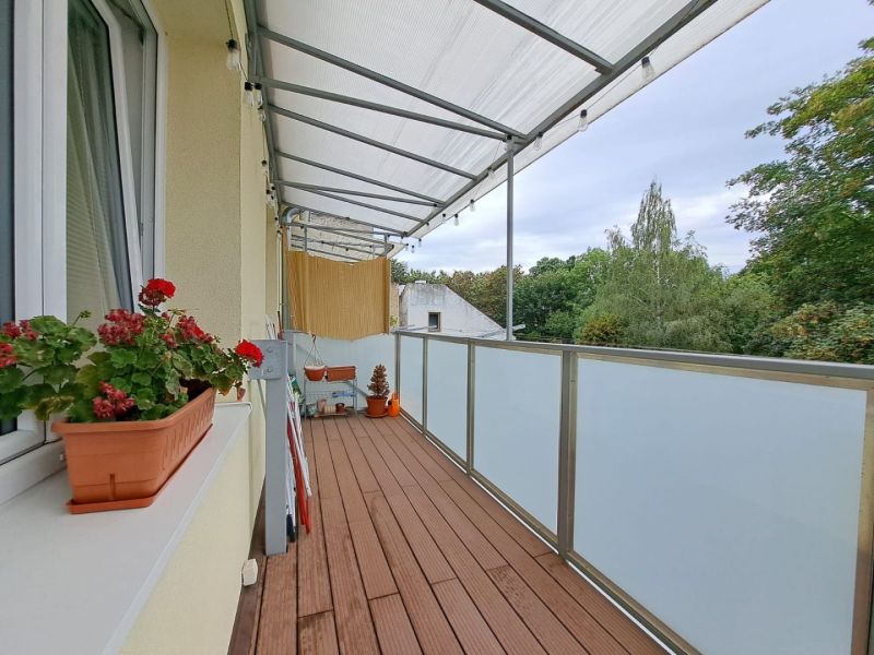 A balcony in a 3-room apartment with a wooden decor floor, flowers, and a view.