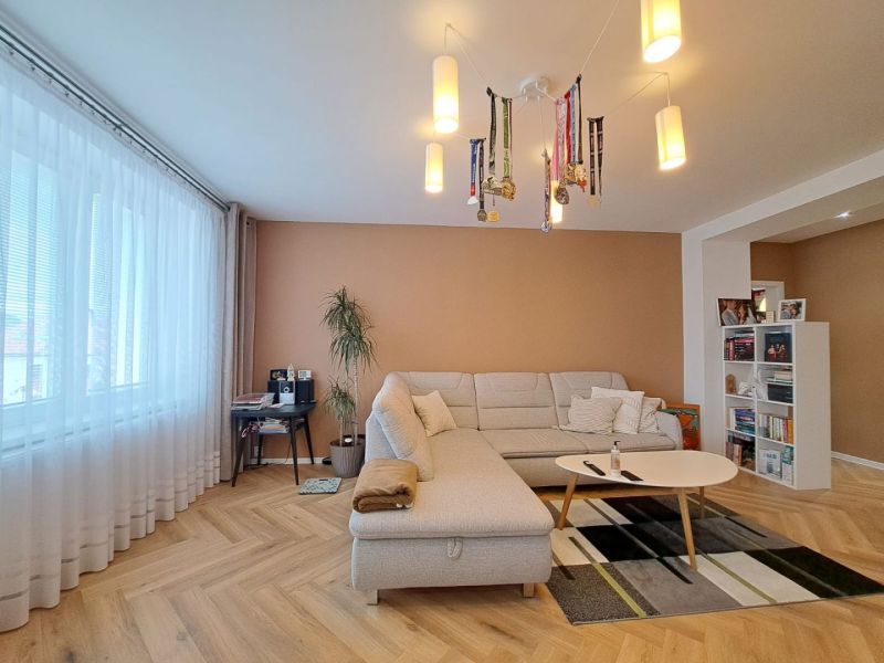 Living room with a white couch, wood-patterned floor, and a bookshelf in a 3-room apartment.