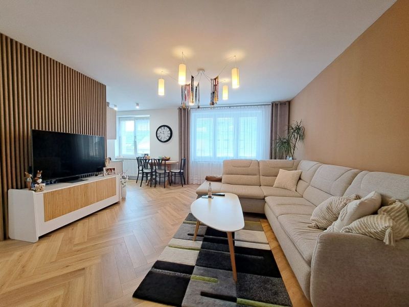Living room in a 3-room apartment with a sofa, wooden decor, and a dining table in the background.