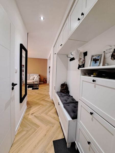 A hallway in a 3-room apartment with white furniture and a wooden decor floor.