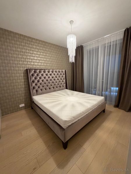 Bedroom in a 2-room apartment with a bed, curtains, and a wooden decor floor.