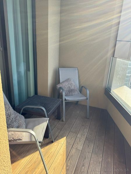 A balcony of a two-room apartment with a wooden decor floor, two chairs, and glass railings.