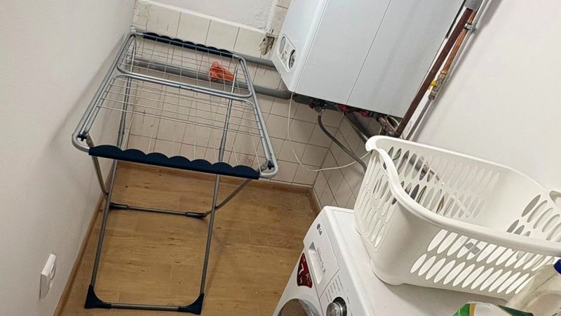 Laundry room in a family house with a washing machine, drying rack, and wooden decor flooring.
