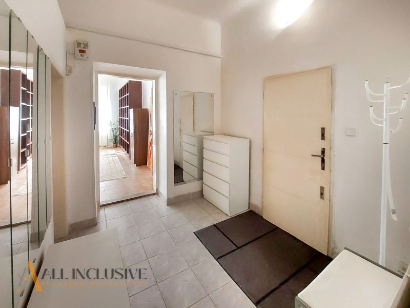 A hallway with white furniture, a mirror, and an entrance to a room in a 2-room apartment.