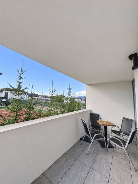 A balcony of a 2-room apartment with seating, a view of greenery, and modern tiles.