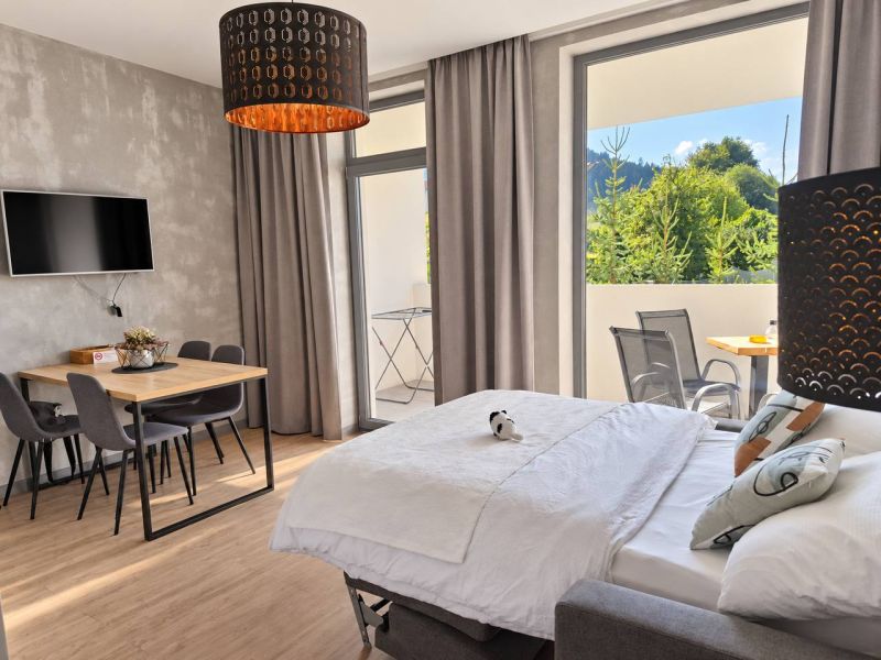 A room in a 2-room apartment with a wooden decor floor, a dining table, and a bed.