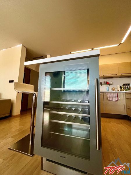 A kitchen in a 3-room apartment with a wine refrigerator and a floor with a wooden decor.