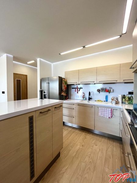 The kitchen of a three-room apartment with a wooden decor floor and light furniture.