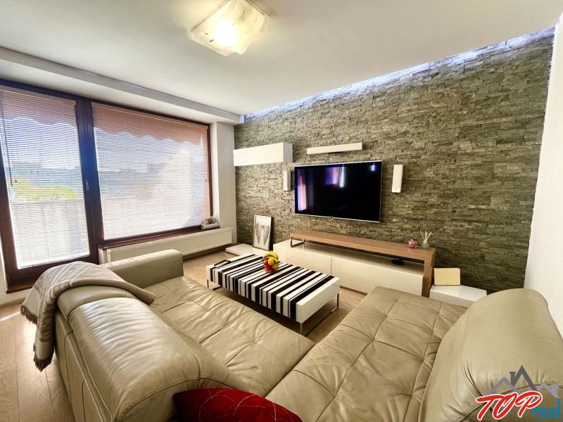 Living room in a 3-room apartment with a leather sofa, stone wall, and floor with a wooden decor.