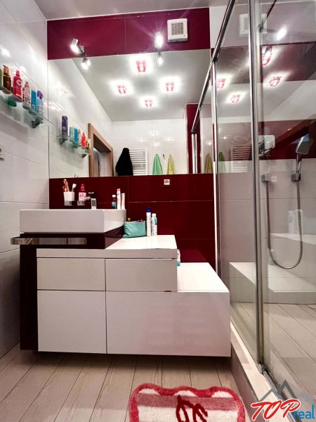 A bathroom with a shower, sink, and shelves in a 3-room apartment.
