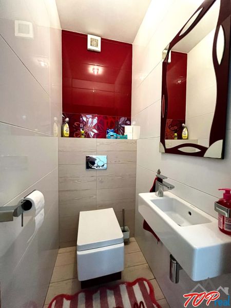 A bathroom in a 3-room apartment with a wall-hung toilet, a sink, and red tiles.