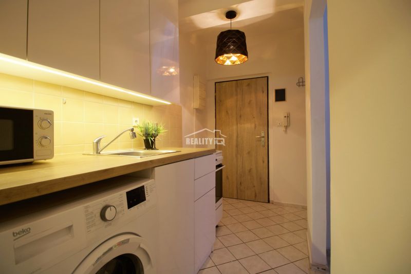A kitchenette in a studio apartment with wooden floor decor and white cabinets.