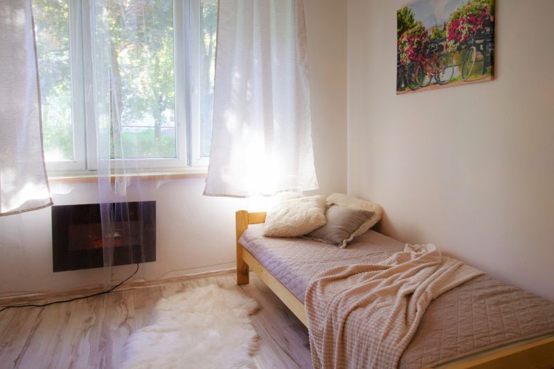 Studio apartment with a bed, blanket, and window, next to a wooden decor counter.
