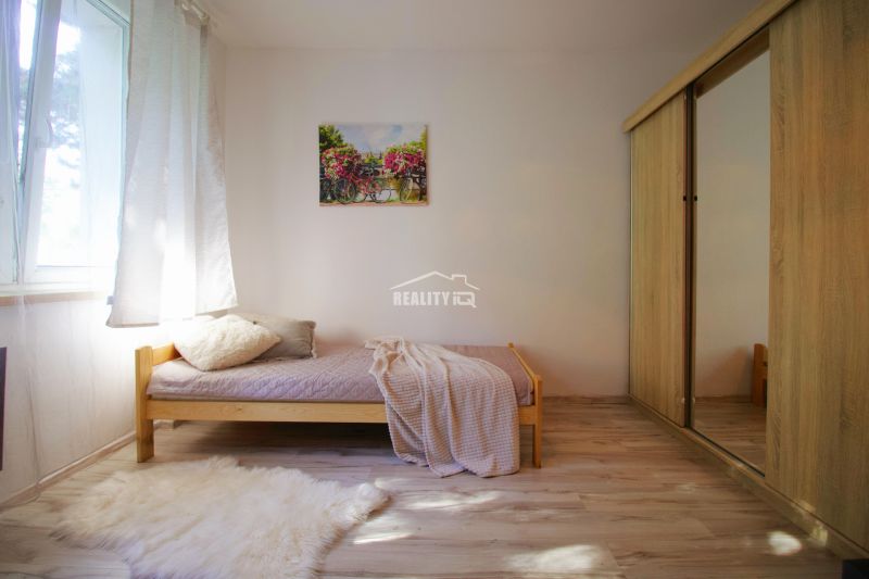 A studio apartment with a simple bed, a wardrobe, and a floor with a wooden decor.