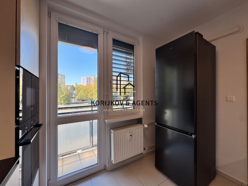 A kitchen with white walls, large windows, and a black refrigerator in a 3-room apartment.