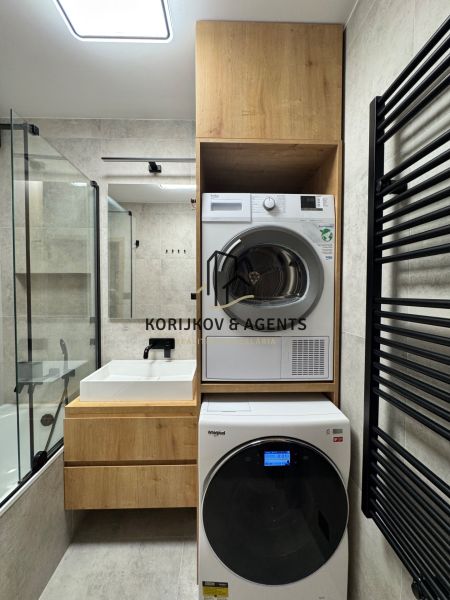A bathroom in a 3-room apartment with a washing machine and dryer, light tiles, wooden decor.