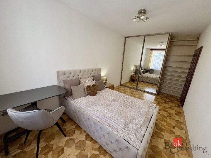 Bedroom in a 3-room apartment with a bed, wardrobe, and wooden decor flooring.