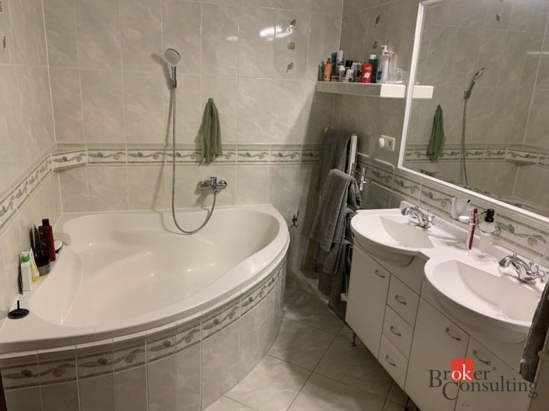 A bathroom with a corner bathtub, double sink, and ceramic tiles in a 3-room apartment.