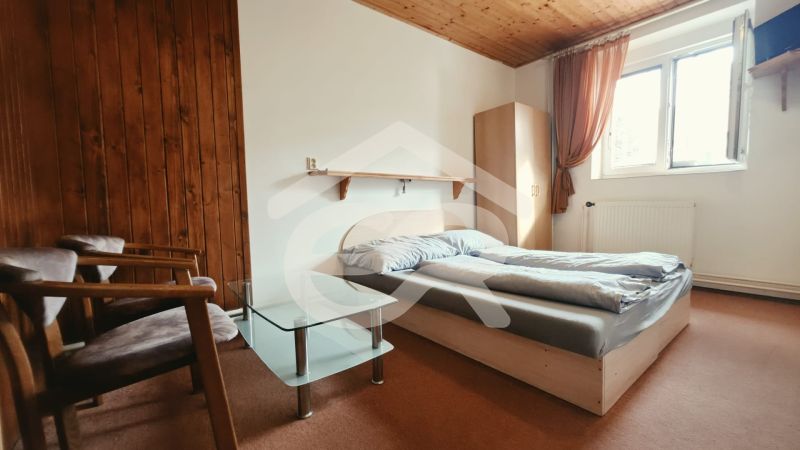 Bedroom of the vacation apartment with a double bed, armchairs, and a window, floor with wooden decor.