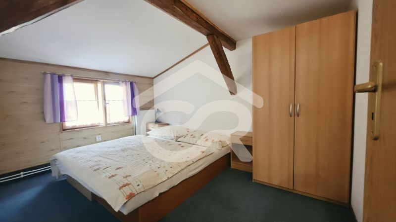 Bedroom in a holiday apartment with wooden beams, a wardrobe, and a bed next to the window.