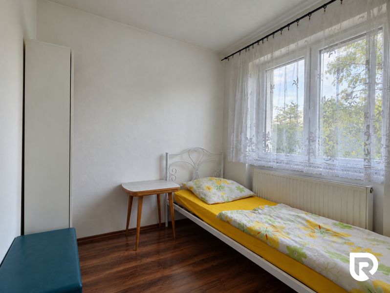 Single room with a bed and a desk, wooden decor flooring, white interior.