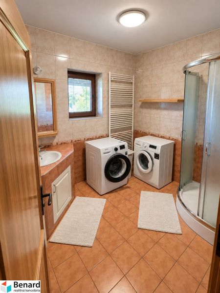 A bathroom in a family house with a washing machine, dryer, and shower enclosure.