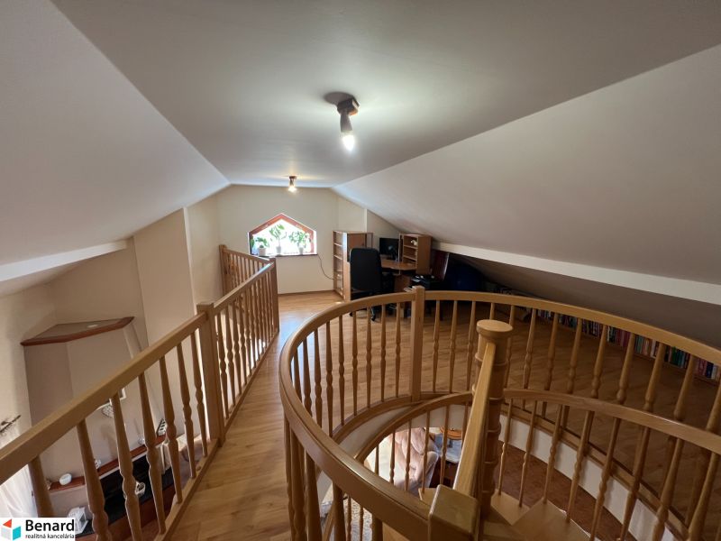 A staircase in the attic of a family house with a wooden decor floor and a work corner.