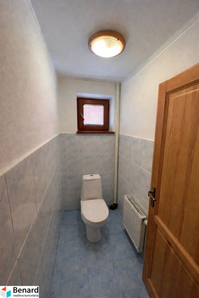 A toilet in a family house with blue tiles and a small window.