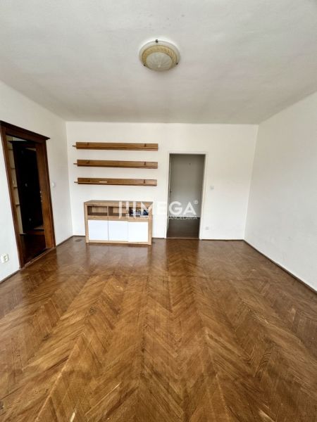 A room in a 3-room apartment with a wooden decor floor and shelves on the wall.