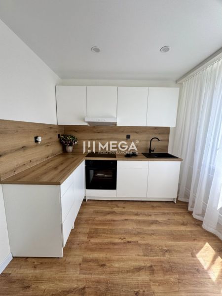 A kitchen with white cabinets, wooden decor, and flooring in a studio apartment.