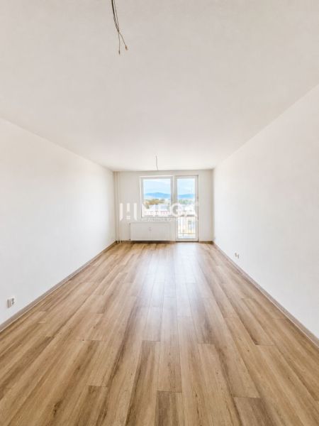 A spacious living room with access to a balcony and a floor with a wooden decor in a 2-room apartment.