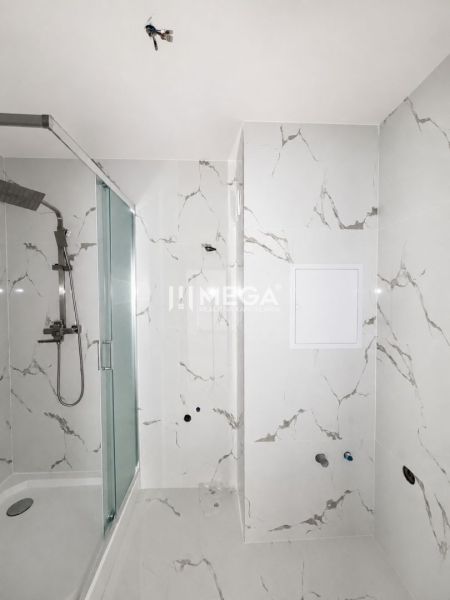 A bathroom with a shower in a two-room apartment with marble tiles.