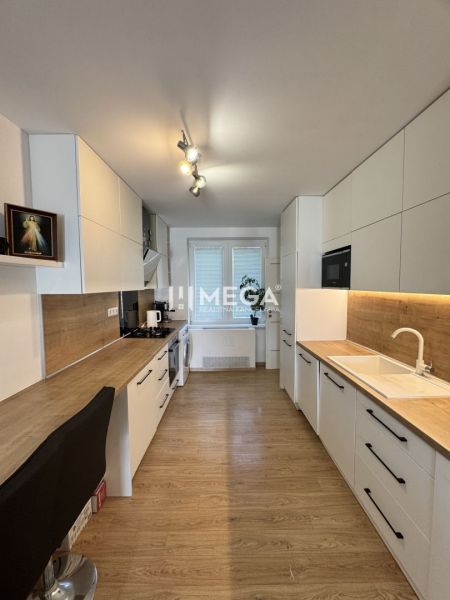 A kitchen in a 3-room apartment with a wooden decor floor and white cabinets.