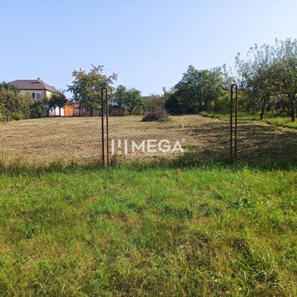 Building plot for sale in Humenné, fenced with a wire fence, house in the background.