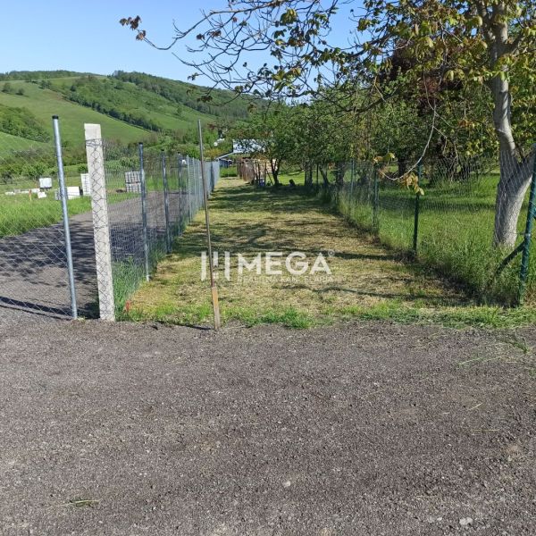 A residential plot in Humenné on a fenced street, surrounded by greenery.