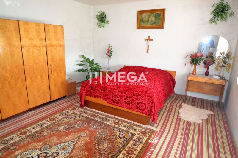 A bedroom in a family house with a red blanket, wooden furniture, and decorative flowers.