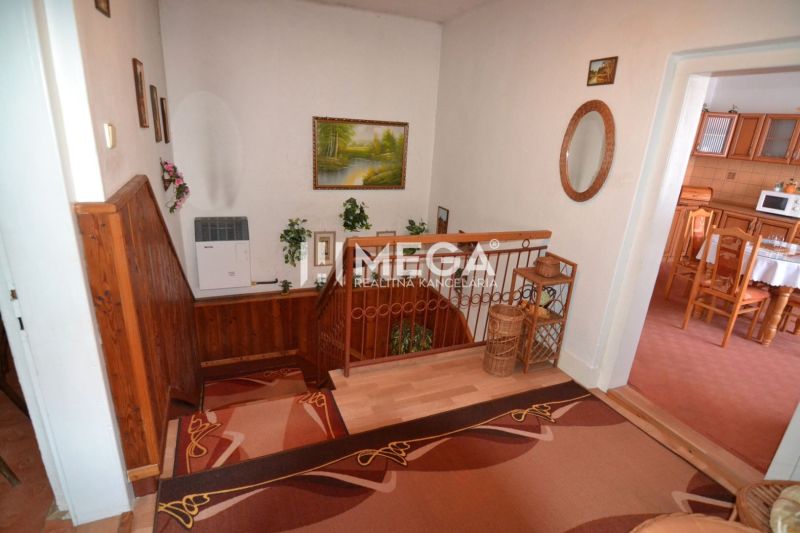 A hallway with carpets and a staircase, a floor with a wooden decor, access to the kitchen.