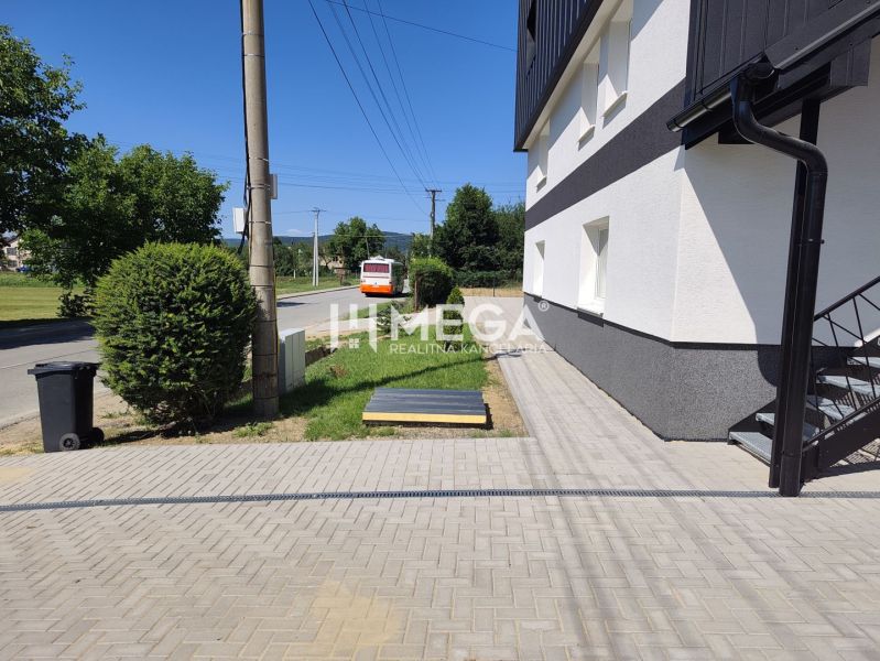 The exterior of a 4-room apartment in Jasenov with a road and a bus, surrounded by greenery.