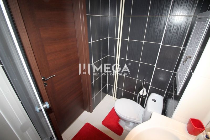Bathroom in a holiday apartment with a shower, toilet, and black tiles.