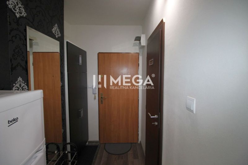 A hallway in a recreational apartment with a wooden decor floor, wallpaper, and a refrigerator.