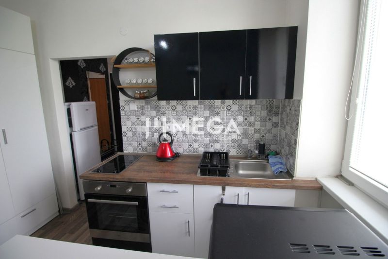 A kitchen in a holiday apartment with a wooden decor floor and geometric tiles on the wall.