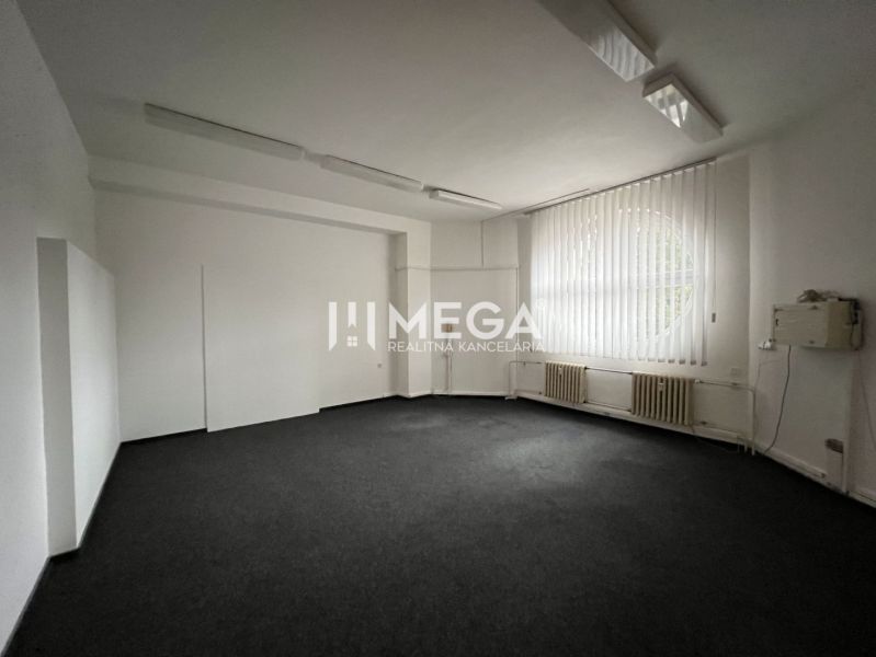 Office space with carpet flooring, a large window, and vertical blinds.