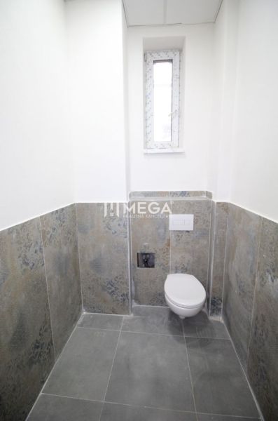 A bathroom in commercial premises with a simple design, featuring a toilet and a narrow window.