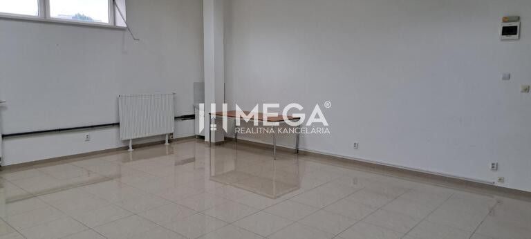 Spacious offices with white walls and tiles, a dining table, a radiator by the window.