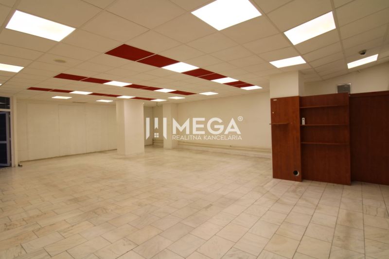 Interior of a commercial space with tiled flooring and ceiling lighting, shelves on the wall.