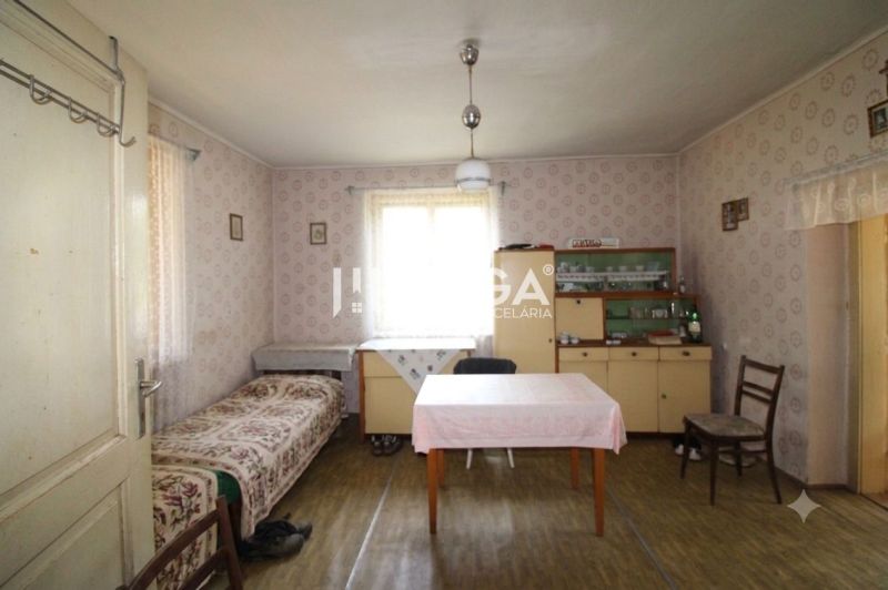A room in a family house with wallpaper, a table, a bed, a display cabinet, and a floor with a wooden decor.