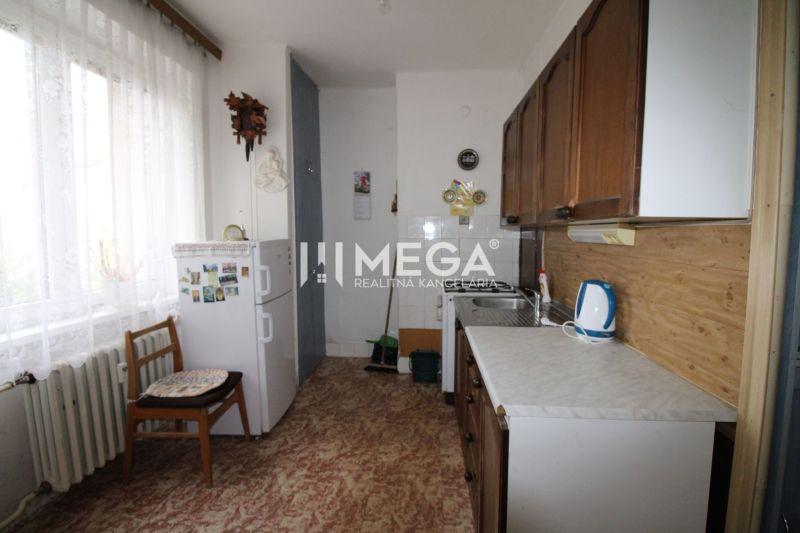 Kitchen in a 2-room apartment with a refrigerator, wooden decor flooring, light curtain.